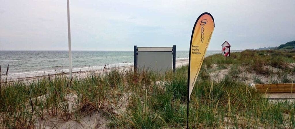 Skruvs gula och orange flagga på en strand med havet i bakgrunden