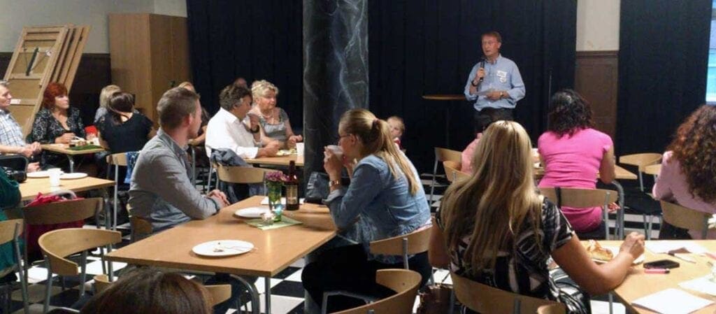 människor som sitter vid bord och lyssnar på en talare
